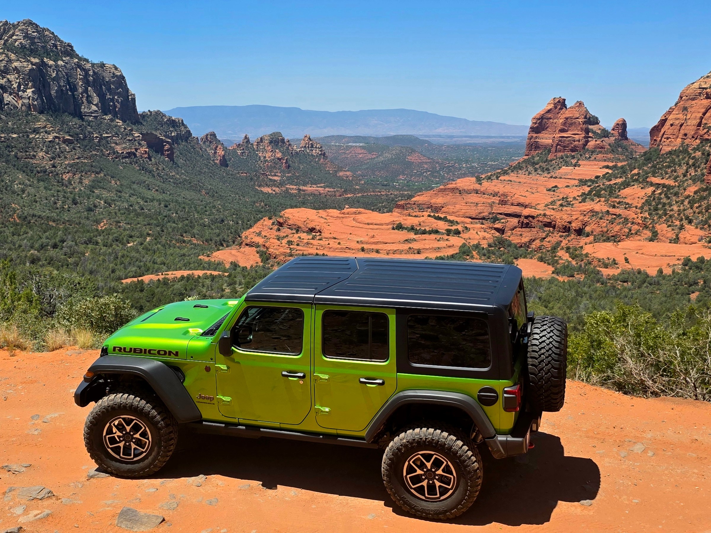 Green Jeep on red rock terrain with canyon and mountains in the background.