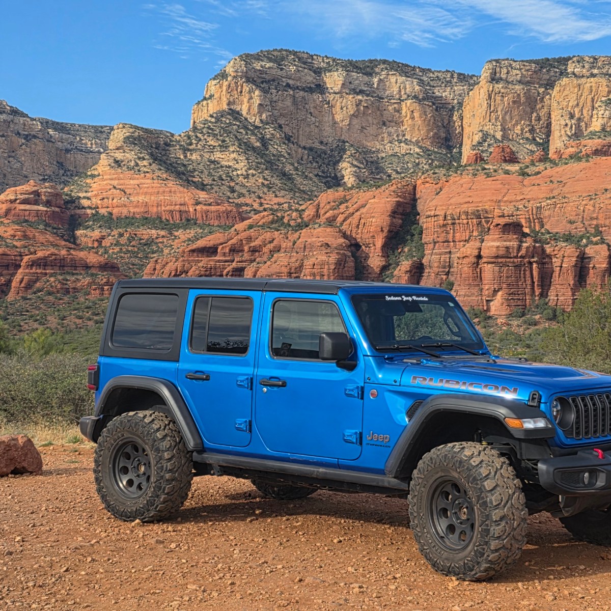 Blue Jeep parked on rocky terrain with red rock cliffs in the background.