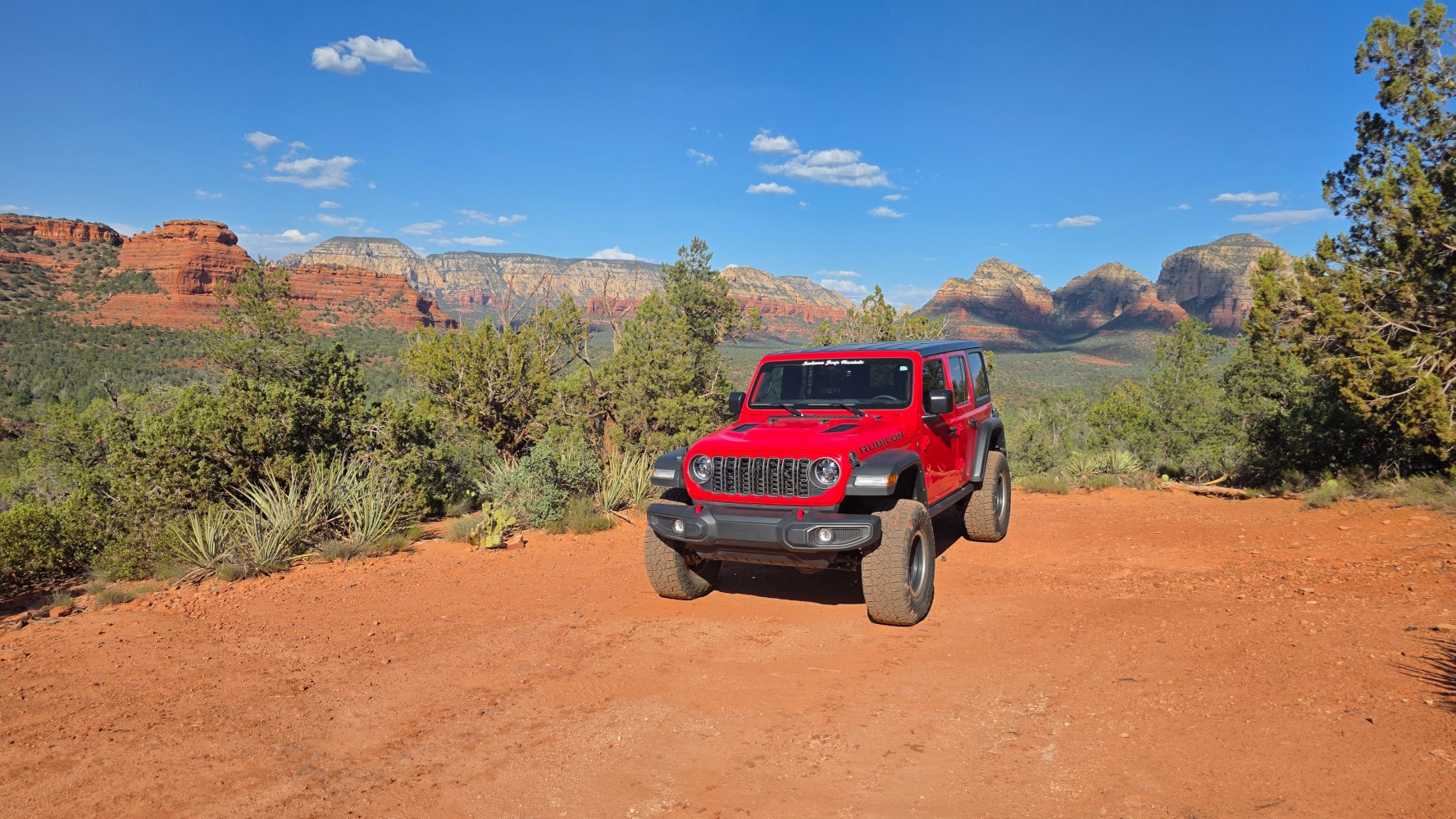 Red SUV on a dirt road with mountains and trees in the background.