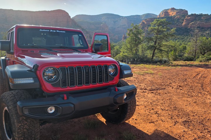 Red Jeep on dirt road near rocky landscape and trees.