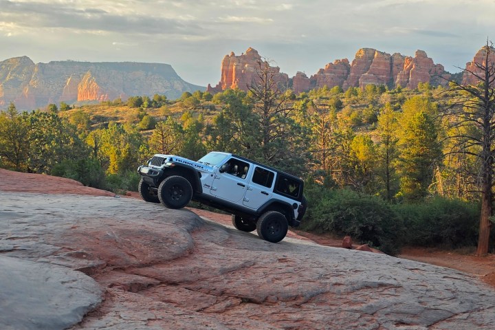 Jeep climbing rocky terrain with red rock formations in the background.