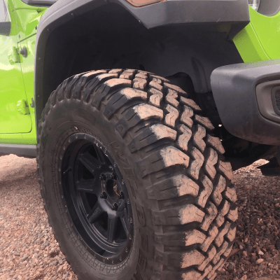 Close-up of a green off-road vehicle with large rugged tires on gravel.