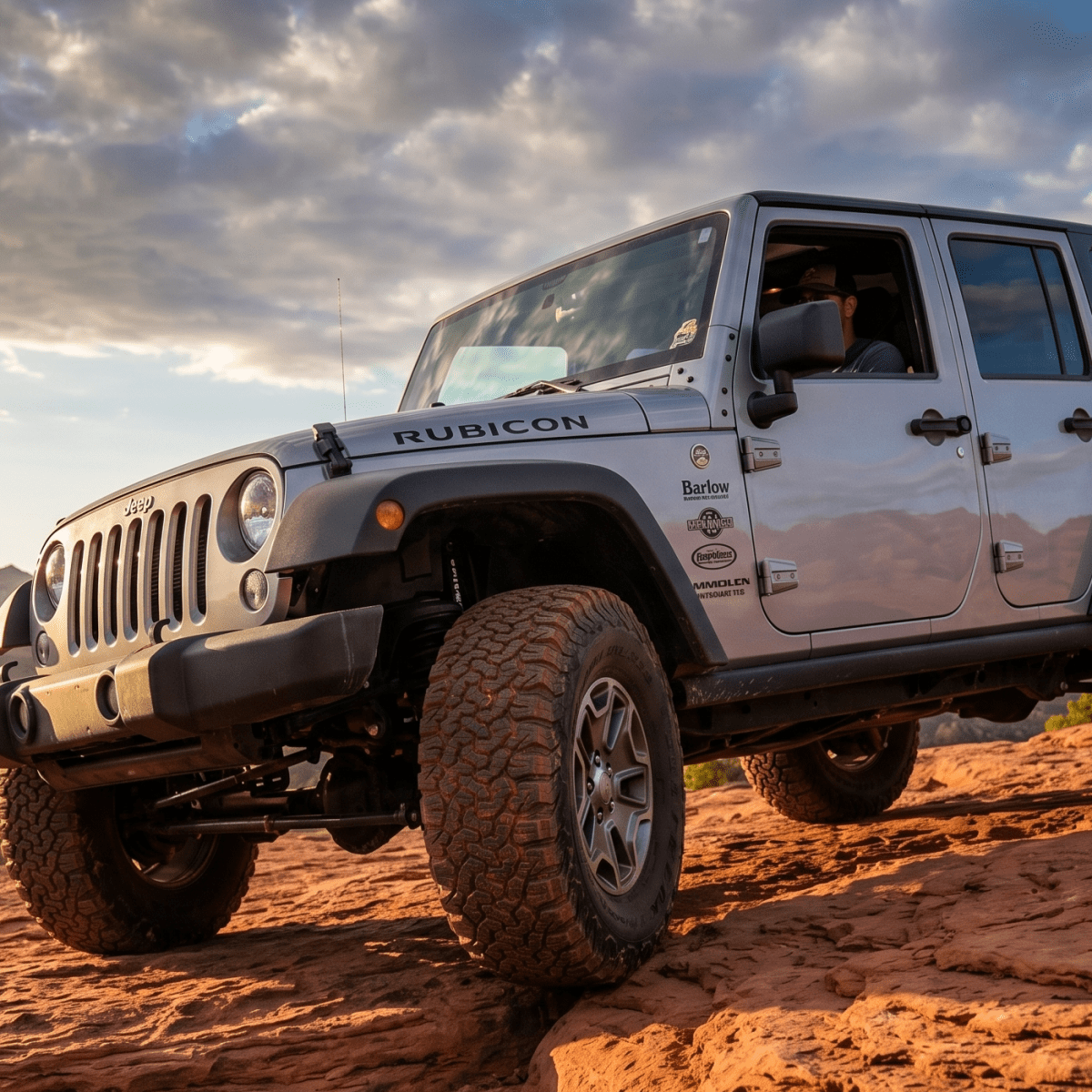 Jeep on rocky terrain with desert landscape and cloudy sky.