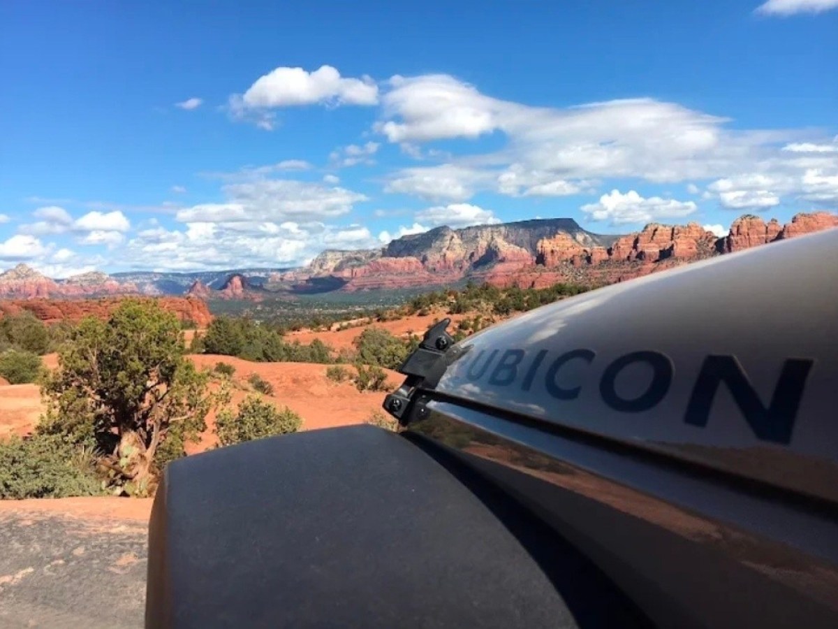 Jeep on a desert trail with red rock formations and a blue sky.