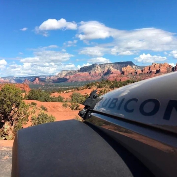 Jeep on a desert trail with red rock formations and a blue sky.