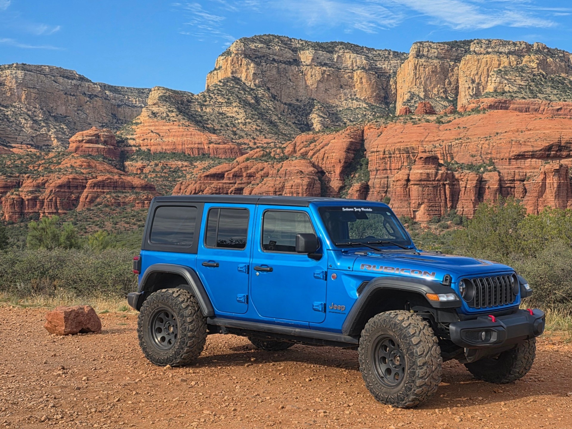 Blue SUV parked on rocky terrain with red rock cliffs in the background.