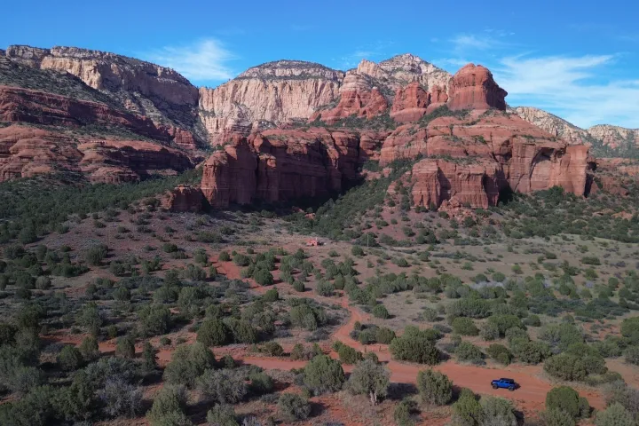 Desert landscape with red rock formations and sparse green vegetation under a blue sky.