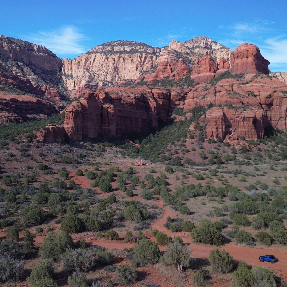 Desert landscape with red rock formations and sparse green vegetation under a blue sky.