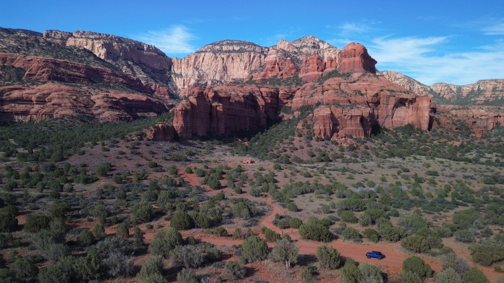 Desert landscape with red rock formations and sparse green vegetation under a blue sky.