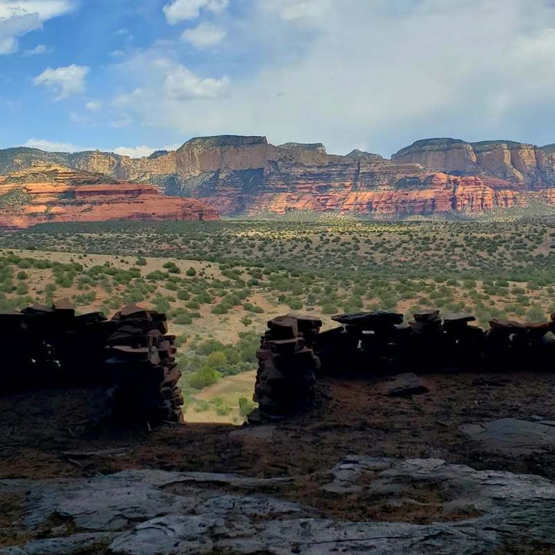 Stone wall overlooking desert landscape with red rock cliffs under a cloudy sky.