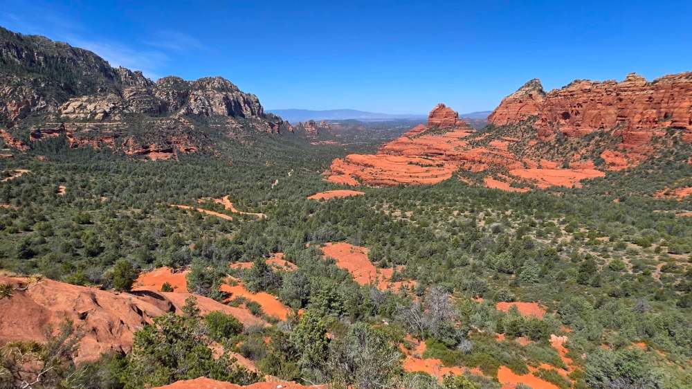 Panoramic view of Sedona's red rock formations and greenery under a clear blue sky.