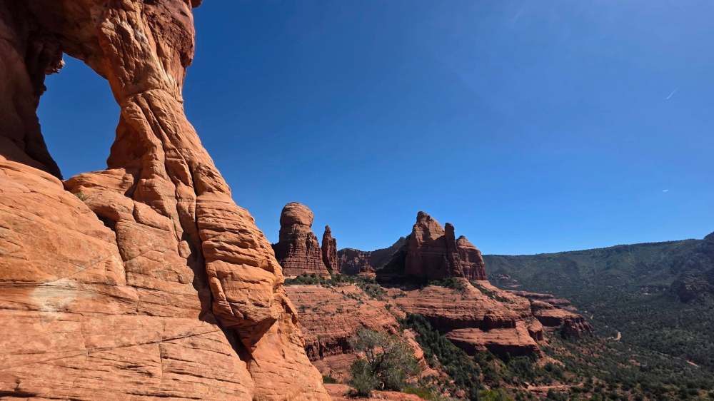 Desert rock formations under a clear blue sky with vegetation.
