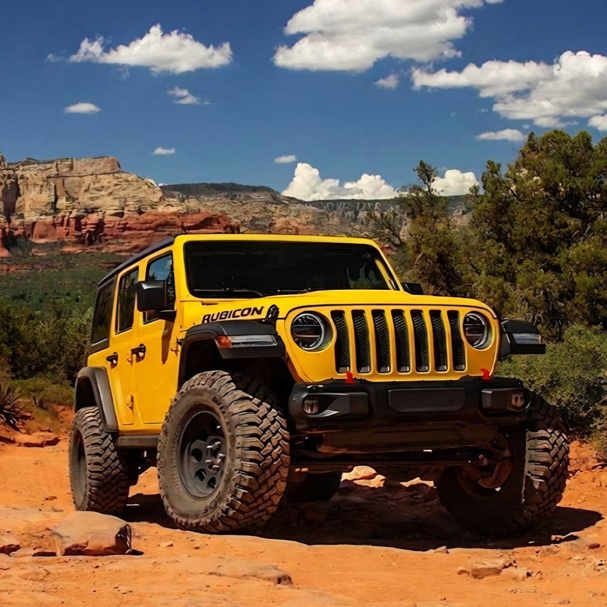 Yellow off-road vehicle on a rocky desert trail with cliffs in the background.
