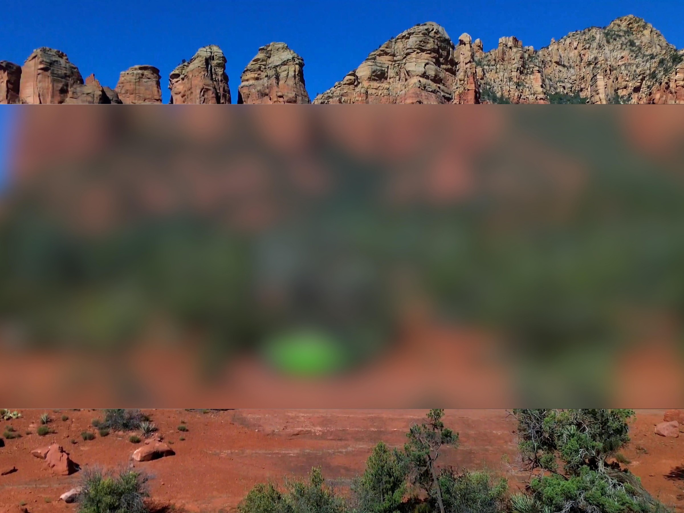 Red rock formations under clear blue sky with blurred foreground.