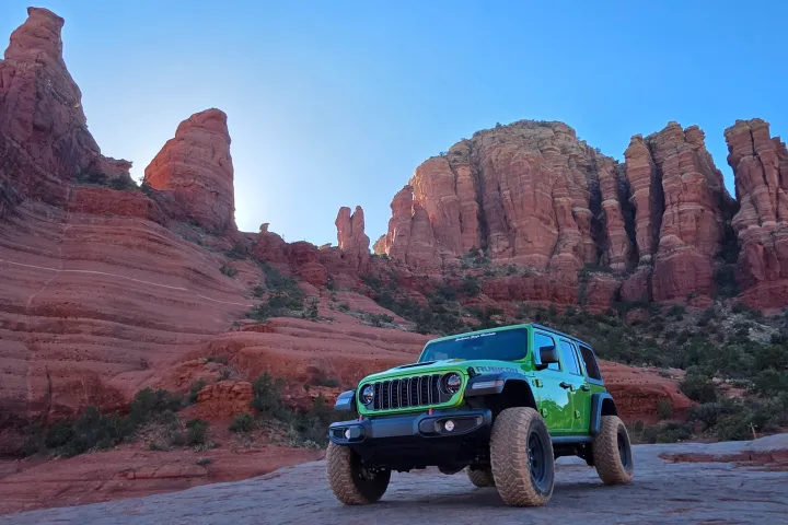 A green off-road vehicle on rocky terrain with red rock formations in the background.