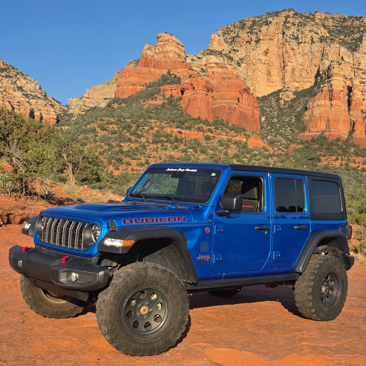Blue off-road vehicle in desert landscape with red rock formations.
