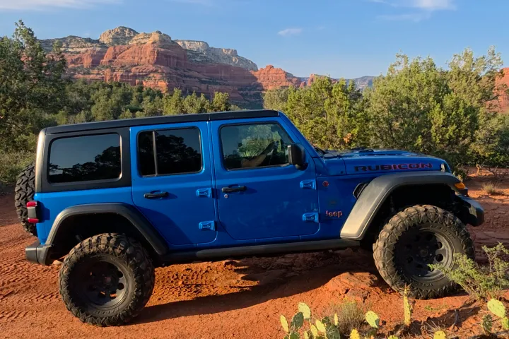 Blue off-road vehicle on a dirt path with red rock formations in the background.