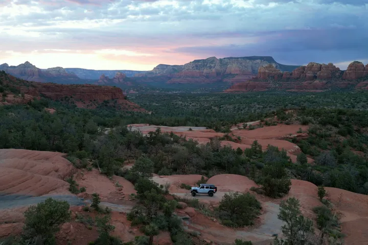 Off-road SUV on a rocky desert landscape with mountains in the background at sunset.