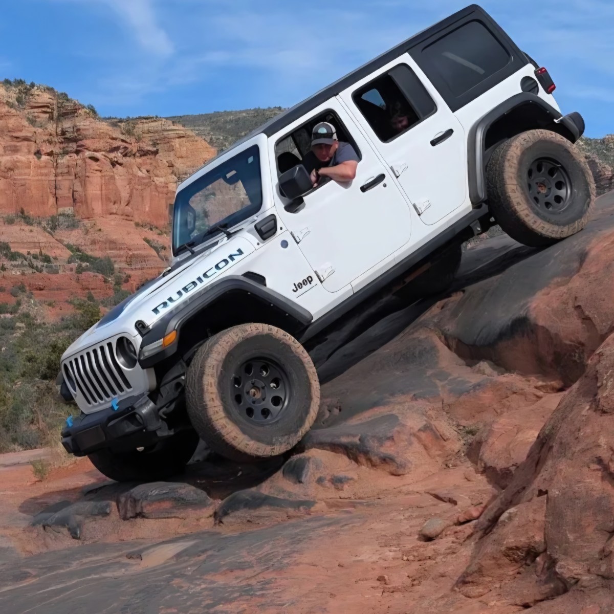 White Jeep descends rocky slope in desert terrain.