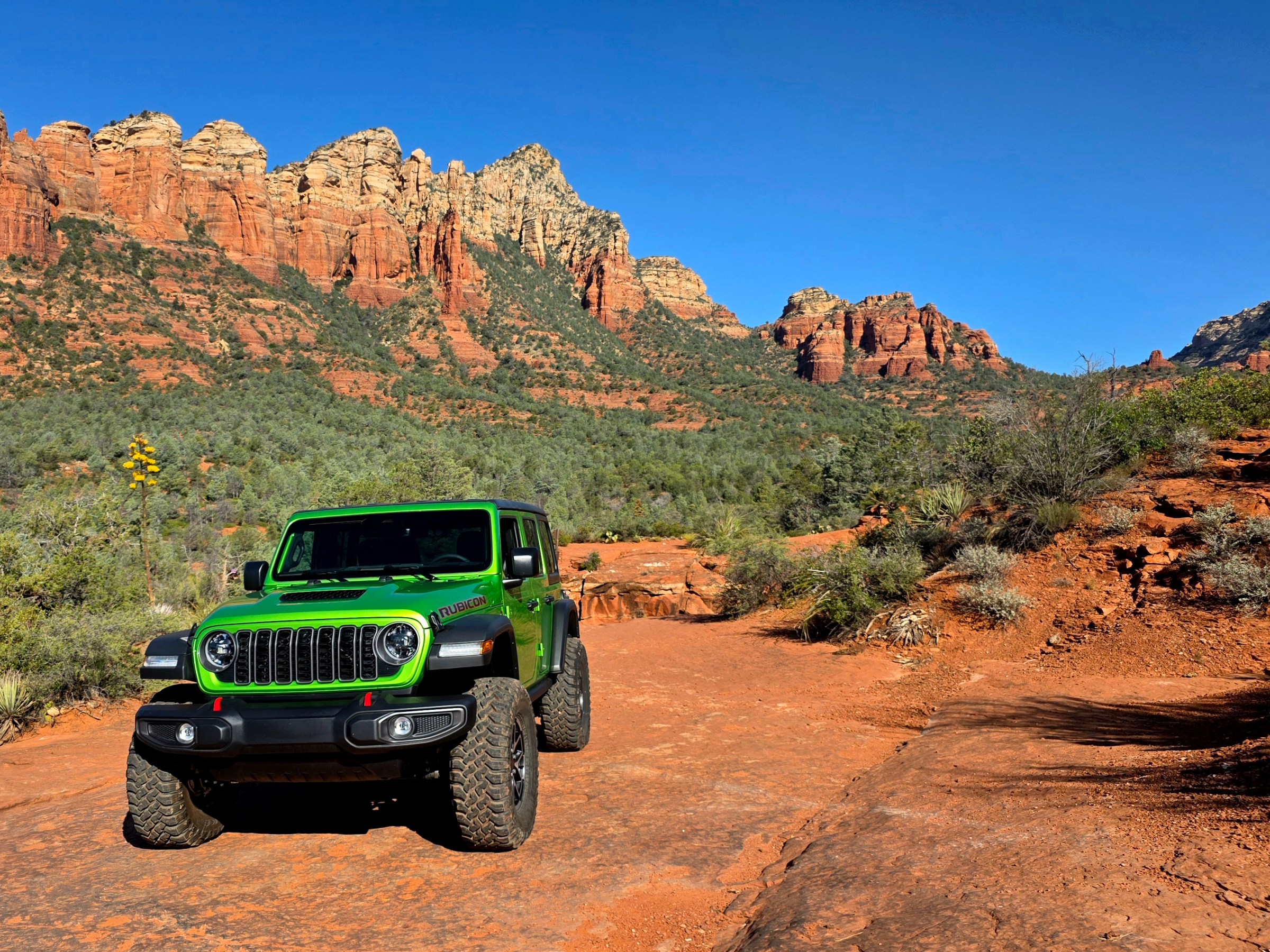 Green SUV on red dirt path amid rocky desert landscape with mountains.