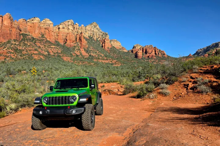Green SUV on red dirt path amid rocky desert landscape with mountains.