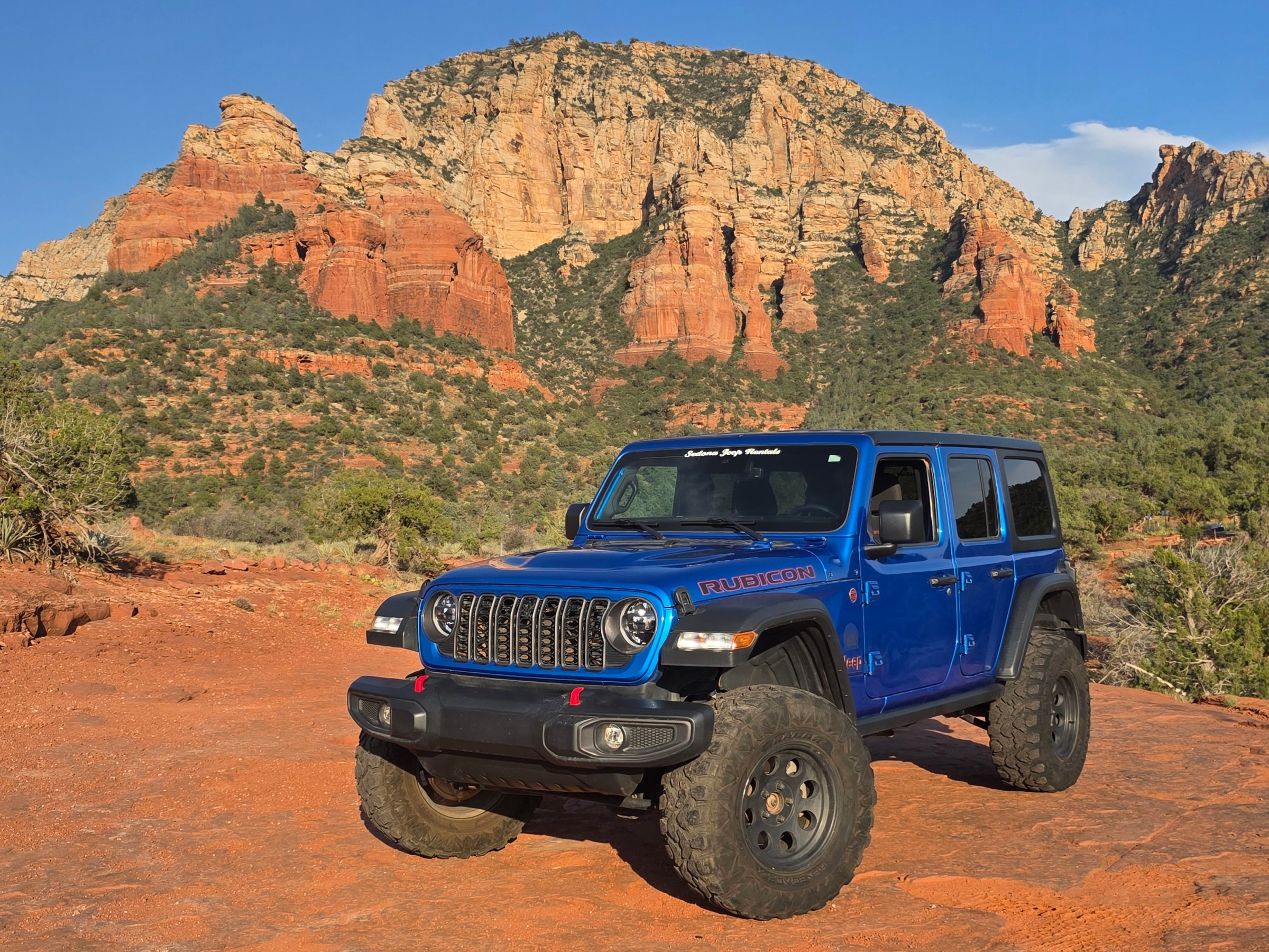Blue SUV driving on a rocky, red desert landscape with large cliffs in the background.