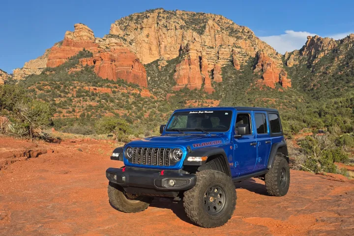 Blue SUV driving on a rocky, red desert landscape with large cliffs in the background.