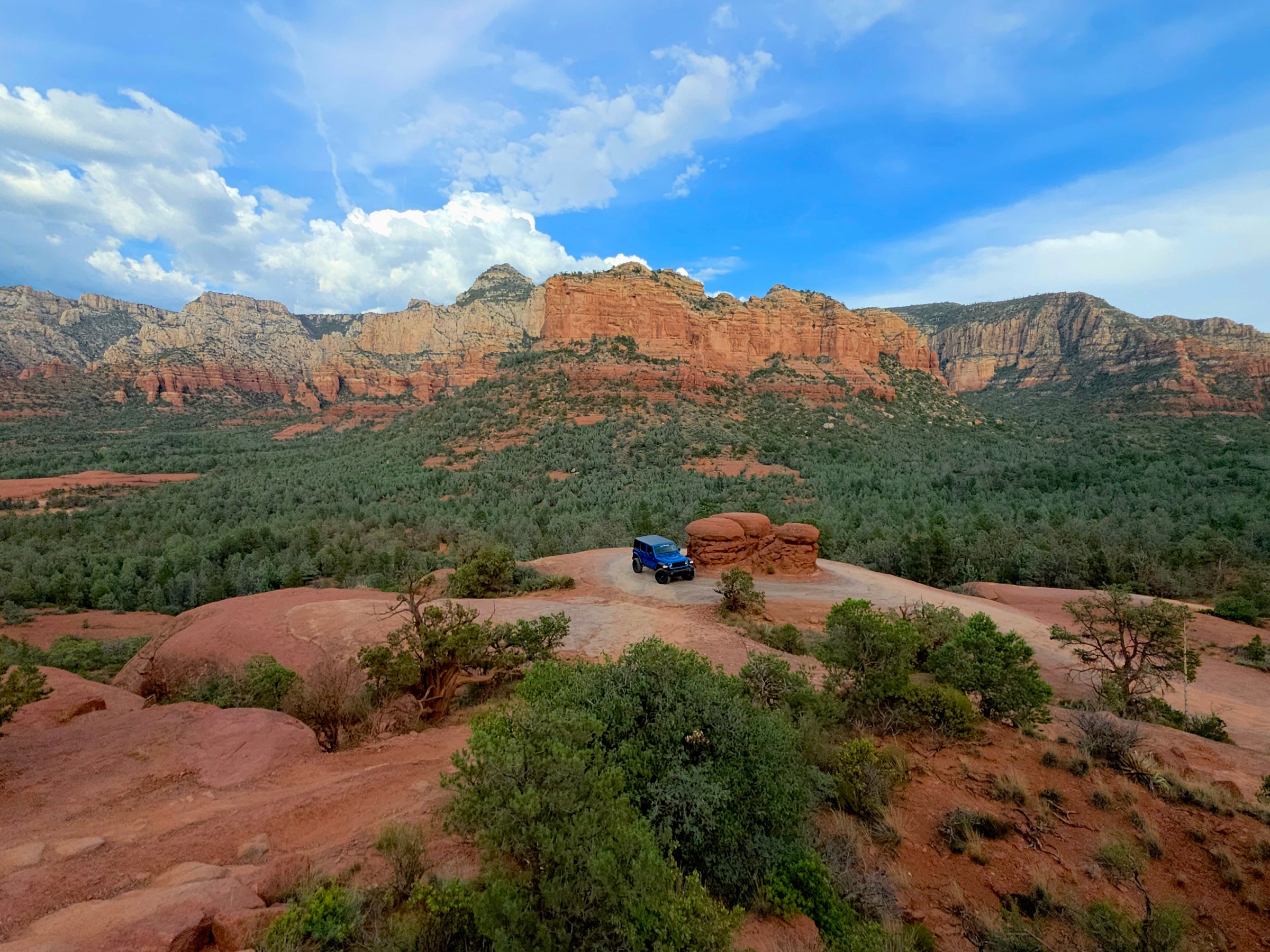 Car parked on a red rock plateau with mountains in the background and a blue sky above.
