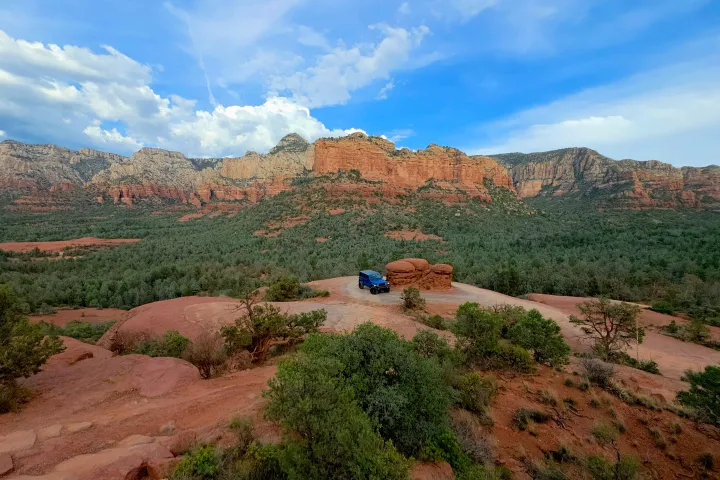 Car parked on a red rock plateau with mountains in the background and a blue sky above.