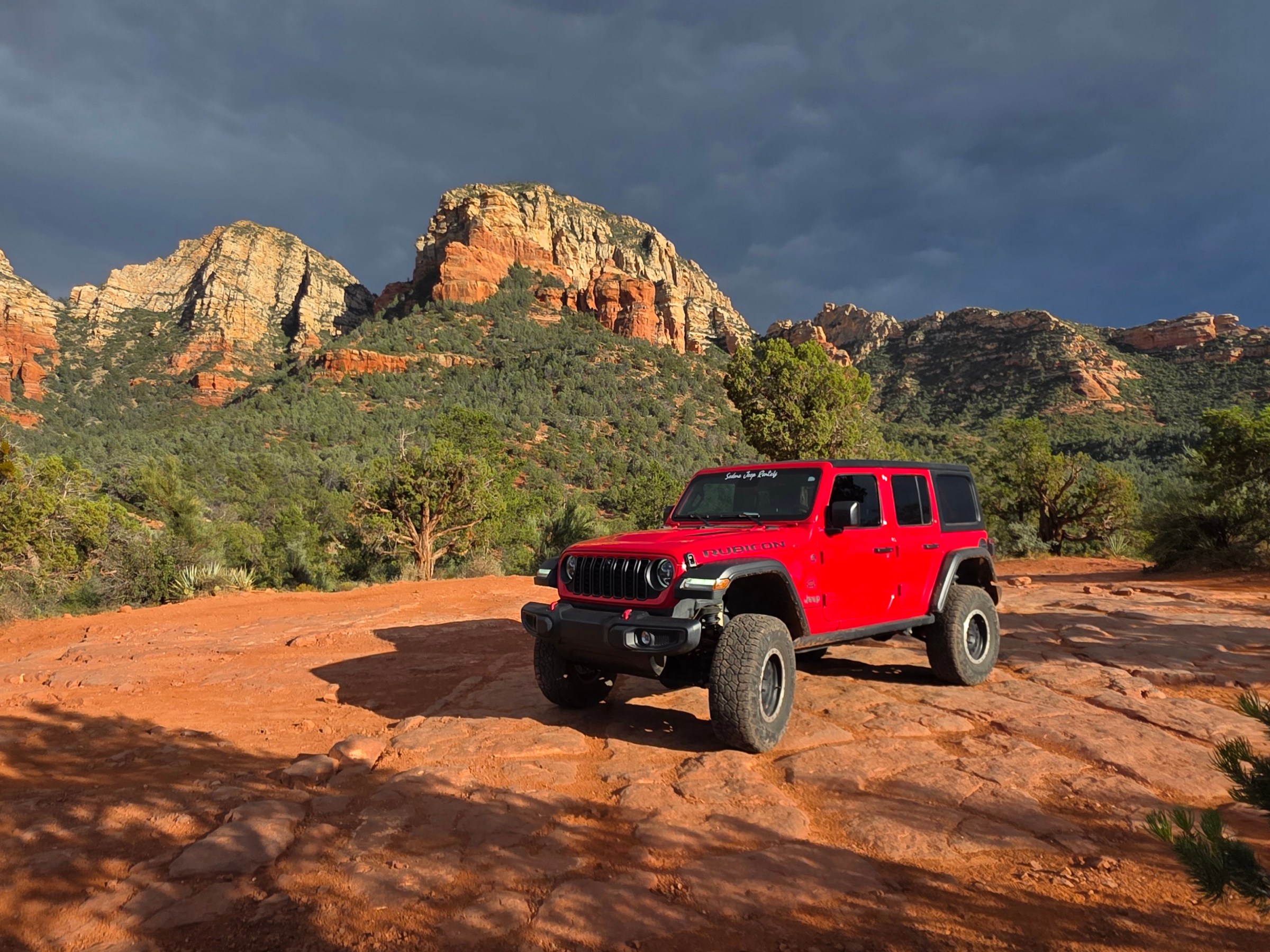Red off-road vehicle on rocky terrain with desert mountains in the background.