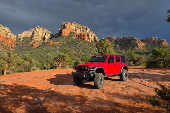 Red off-road vehicle on rocky terrain with desert mountains in the background.