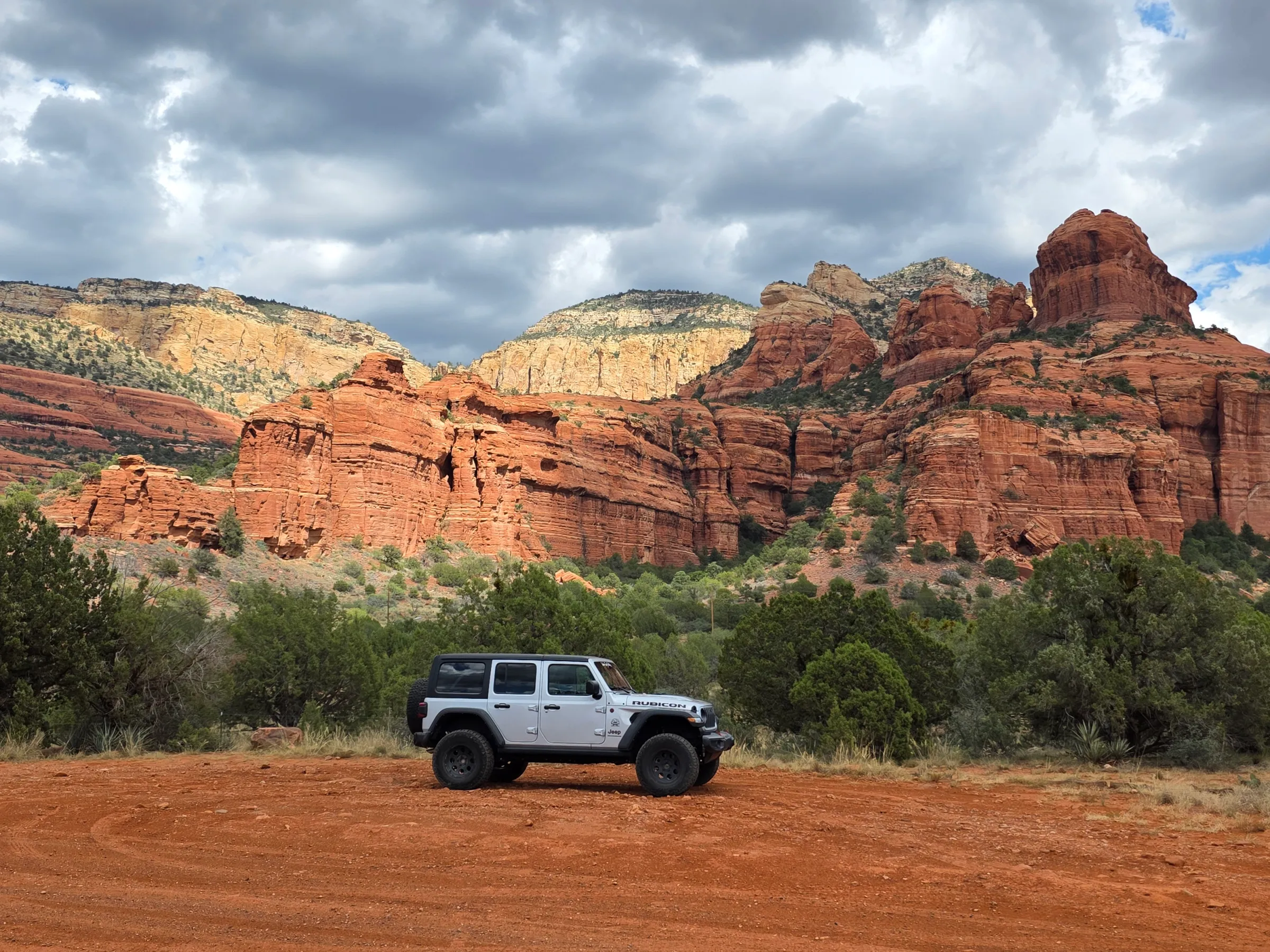 SUV parked on dirt with red rock formations and cloudy sky in background.