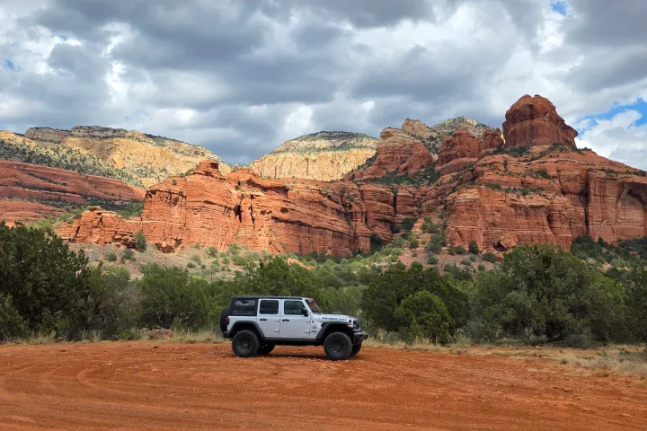 SUV parked on dirt with red rock formations and cloudy sky in background.