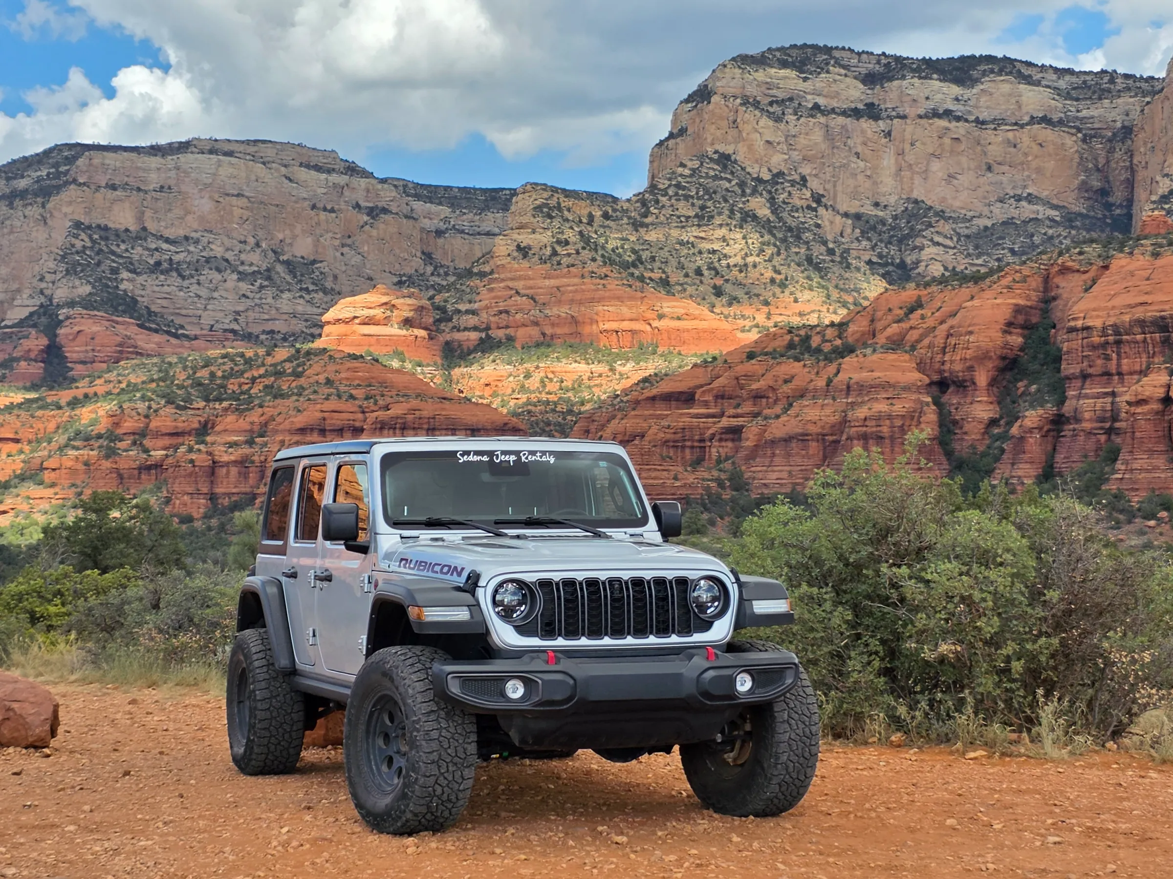 Gray off-road vehicle in desert landscape with red rock cliffs.
