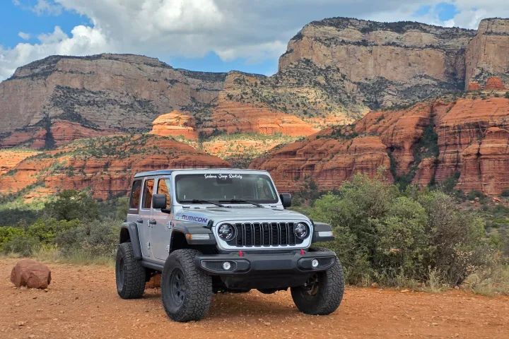 Gray off-road vehicle in desert landscape with red rock cliffs.
