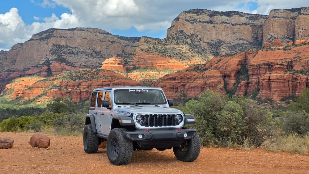Gray off-road vehicle in desert landscape with red rock cliffs.