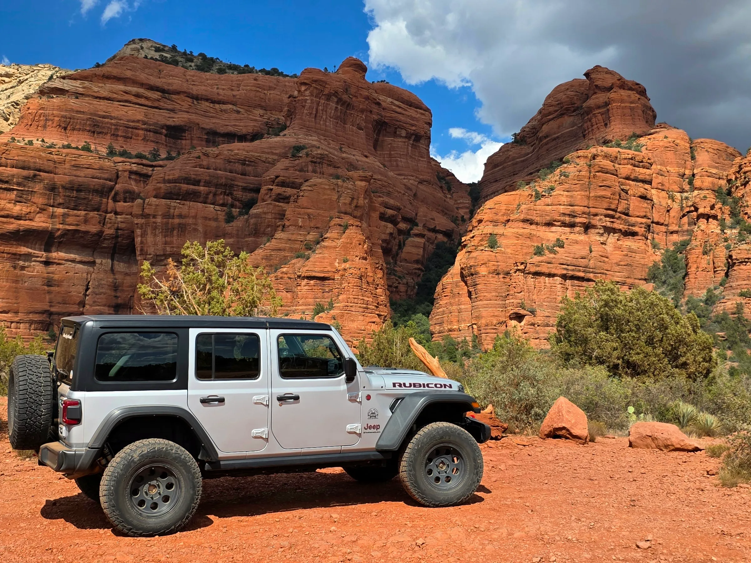 Off-road vehicle parked on red dirt near large red rock formations.