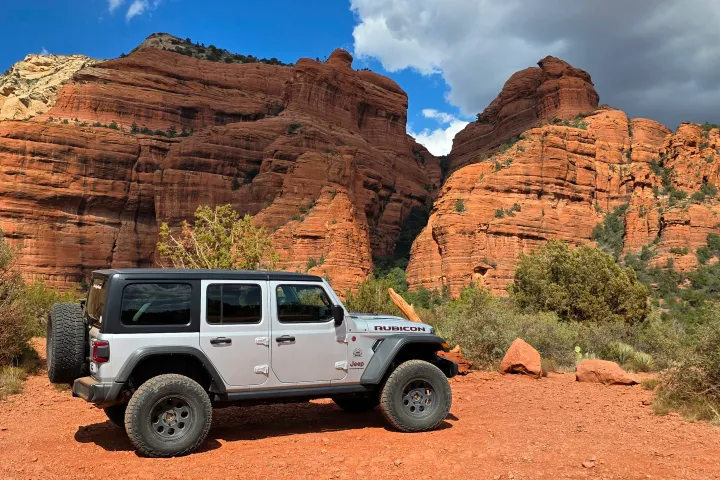 Off-road vehicle parked on red dirt near large red rock formations.