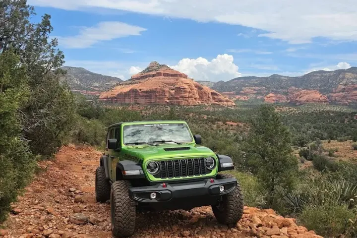 Green off-road vehicle on rocky trail with red rock formations in the background.