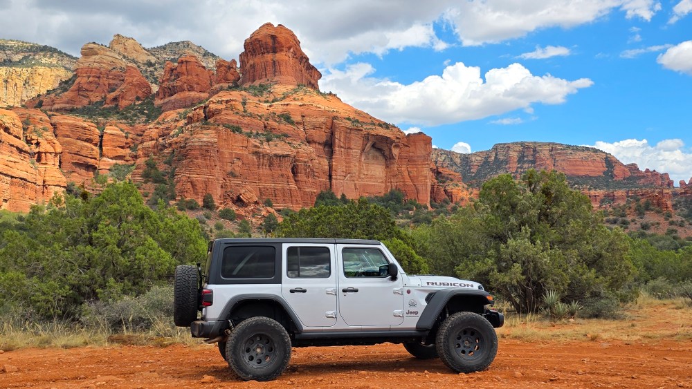SUV parked with red rock formations in the background on a sunny day.