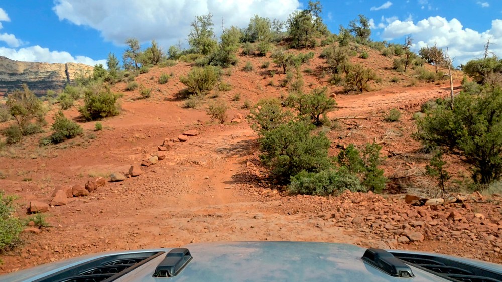 Off-road path on rocky terrain with shrubs and blue sky in the background.