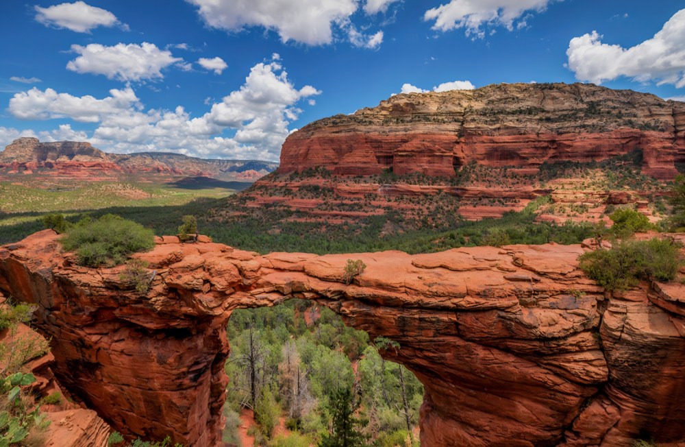 Red rock arch with scenic canyon view under blue sky and clouds.