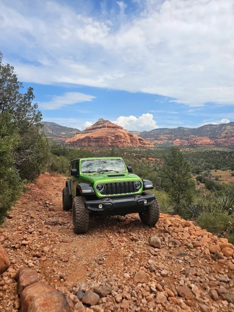 Green Jeep off-road in rocky desert landscape with red rock formations.